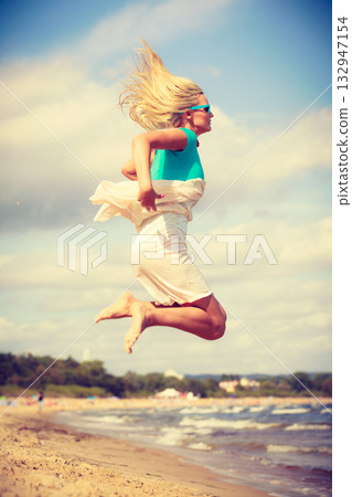 Blonde woman wearing dress playing jumping on beach Blonde woman wearing dress playing jumping on beach 132947154
