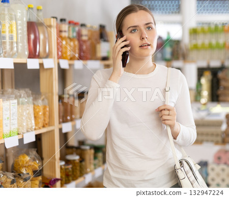 Girl shopping in grocery supermarket and talking on mobile phone Girl shopping in grocery supermarket and talking on mobile phone 132947224