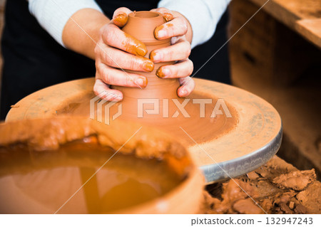 Hands of professional potter molding clay on pottery wheel Hands of professional potter molding clay on pottery wheel 132947243