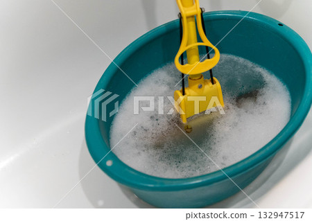 Bright turquoise basin filled with soapy water, featuring a yellow cleaning tool submerged, illustrating the process of household cleaning and maintenance with vibrant colors Bright turquoise basin filled with soapy water, featuring a yellow cleaning tool submerged, illustrating the process of household cleaning and maintenance with vibrant colors 132947517