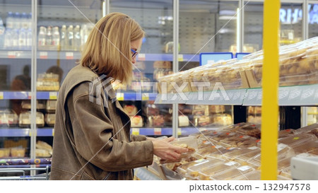 Customer choosing from a selection of packaged bread in a supermarket bakery section, making decisions among a range of baked goods 132947578