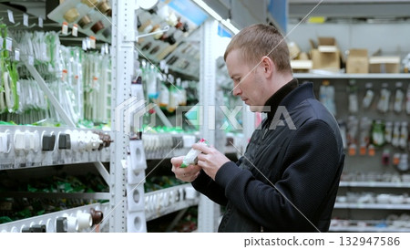 A man in a hardware store, choosing electrical wires. Electrician carefully examines the packaging of an electrical product to choose the best option for his project A man in a hardware store, choosing electrical wires. Electrician carefully examines the packaging of an electrical product to choose the best option for his project 132947586