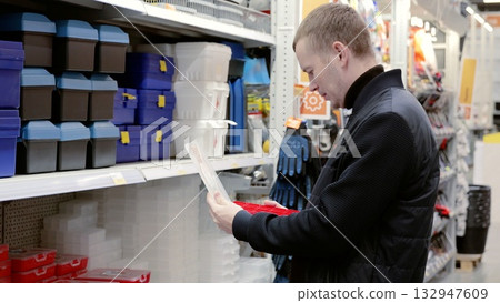 A man in a hardware store choosing a toolbox. Handyman browsing through toolbox options at a hardware store, comparing various models and sizes while holding a red toolbox 132947609