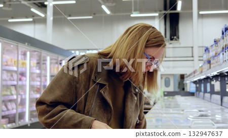 Young woman making informed choices by carefully reading food labels while selecting frozen products in a supermarket refrigerator section Young woman making informed choices by carefully reading food labels while selecting frozen products in a supermarket refrigerator section 132947637