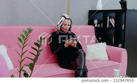Woman with foil in her hair using smartphone while waiting for hair color to process in contemporary salon 132947658