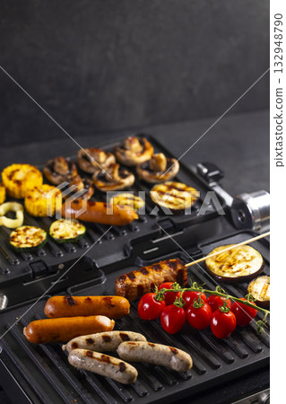 Grilling sausages and vegetables on electric indoor grill 132948790