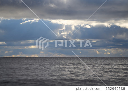 Overcast sky above calm sea horizon with sunlight filtering through clouds. Overcast sky above calm sea horizon with sunlight filtering through clouds. 132949586