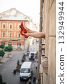 Close-up of female legs with red shoes of high heels. The woman is raising her feet through the window 132949944