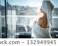 Back view of young woman with towel on her head looking out the window 132949945