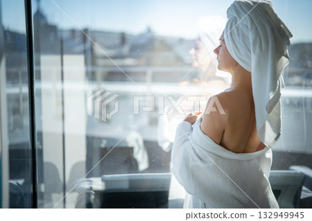 Back view of young woman with towel on her head looking out the window Back view of young woman with towel on her head looking out the window 132949945