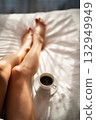 Close-up of female legs with cup of coffee on bed. 132949949
