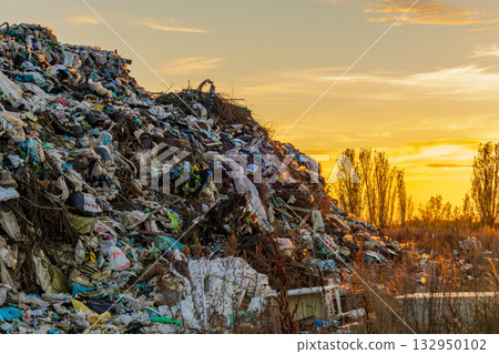 A vast landfill filled with garbage and waste sits under a vibrant sunset sky, highlighting the impact of pollution on the environment 132950102