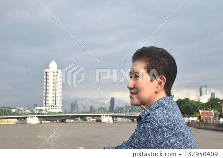 Asian elder woman looking at landscape view of Cho phraya river in Thailand on rainy day 132950409