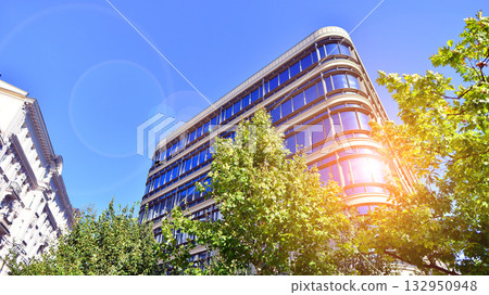 Modern luxury office building.The structure features a glass and concrete walls, showcasing contemporary architecture. The green surroundings of office buildings. Trees and shrubs in the city. Modern luxury office building.The structure features a glass and concrete walls, showcasing contemporary architecture. The green surroundings of office buildings. Trees and shrubs in the city. 132950948