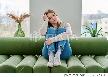 Unhappy upset young woman sitting on sofa at home, face close-up Unhappy upset young woman sitting on sofa at home, face close-up 132952381