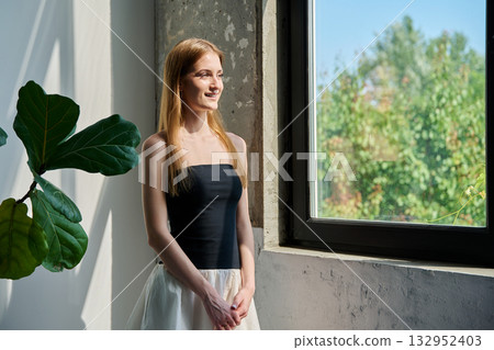 Portrait of smiling dreamy young woman, profile view near window 132952403
