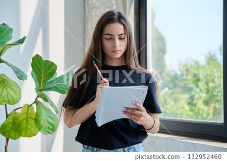 Portrait of teenage college student girl with notebook pencil at home near window Portrait of teenage college student girl with notebook pencil at home near window 132952460