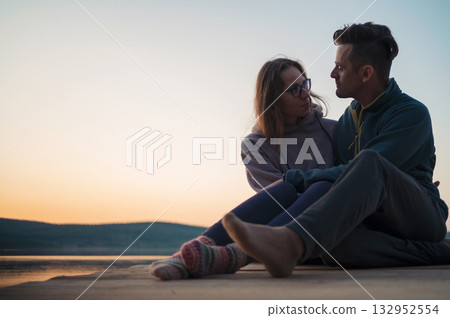 Couple Sitting by Lake at Sunset Embracing Couple Sitting by Lake at Sunset Embracing 132952554