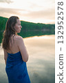 Woman Wrapped in Towel Relaxing by Lake at Sunset 132952578