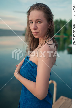 Woman Wrapped in Towel Relaxing by Lake at Sunset 132952583