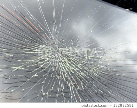 Close Up of a Shattered Windshield Showing Radial Cracks and Broken Glass Damage on Car 132952591