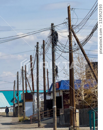 Row of weathered utility poles with tangled wires lining a quiet street scene Row of weathered utility poles with tangled wires lining a quiet street scene 132952593