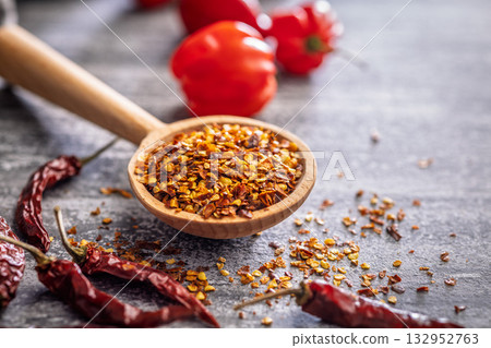 Red chili peppers flakes. Milled spicy peppers on wooden scoop on kitchen table. Red chili peppers flakes. Milled spicy peppers on wooden scoop on kitchen table. 132952763