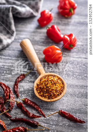 Red chili peppers flakes. Milled spicy peppers on wooden scoop on kitchen table. 132952764