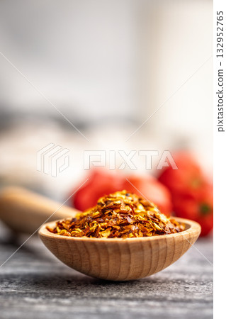 Red chili peppers flakes. Milled spicy peppers on wooden scoop on kitchen table. 132952765