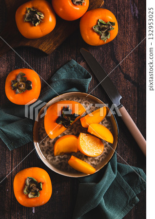 Pieces and halves of persimmon fruit on a plate and on a table top and vertical view 132953025