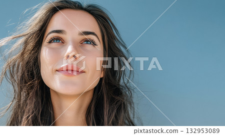 Bright sunlight highlights a woman smiling with flowing hair, capturing a moment of joy and serenity outdoors 132953089