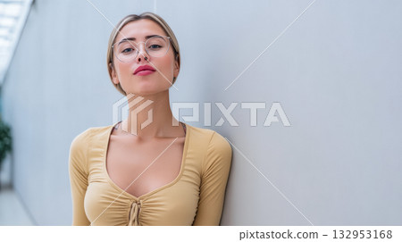 Young woman poses confidently against a neutral wall in a modern indoor space while wearing stylish glasses 132953168