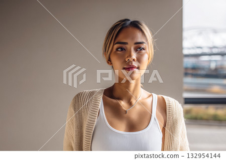 Young woman in cozy sweater looking thoughtfully out a window at a modern urban setting Young woman in cozy sweater looking thoughtfully out a window at a modern urban setting 132954144