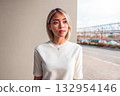 Young woman in casual outfit poses confidently against urban backdrop during afternoon light 132954146