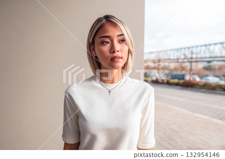Young woman in casual outfit poses confidently against urban backdrop during afternoon light 132954146