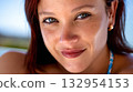 Young woman with blue eyes and freckles smiles in natural light during a sunny day at the beach 132954153