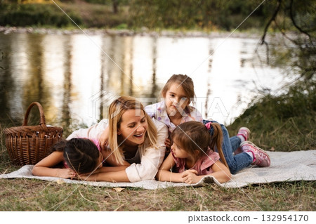 Mother and daughters having fun at a picnic by the river Mother and daughters having fun at a picnic by the river 132954170