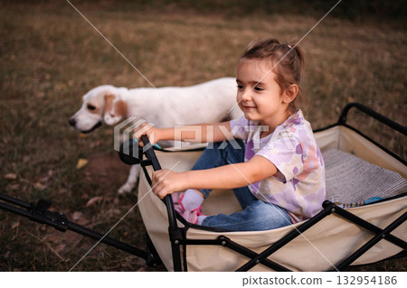 Little girl enjoying a wagon ride with her dog in the park Little girl enjoying a wagon ride with her dog in the park 132954186