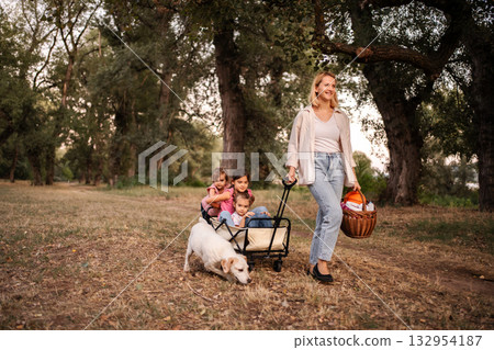 Mother pulling daughters and dog in wagon through park Mother pulling daughters and dog in wagon through park 132954187