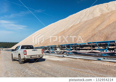 Bright sunlight illuminates open industrial potassium mining site blue conveyor structures silver pickup truck car dusty ground. Steel constructions contrast with light rocks and clear blue sky Bright sunlight illuminates open industrial potassium mining site blue conveyor structures silver pickup truck car dusty ground. Steel constructions contrast with light rocks and clear blue sky 132954214