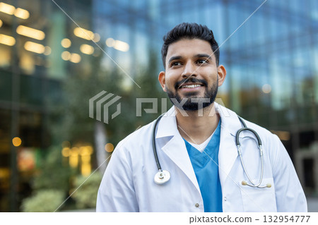 Confident medical professional wearing white coat and stethoscope smiles while looking away from the camera and standing outside modern hospital building Confident medical professional wearing white coat and stethoscope smiles while looking away from the camera and standing outside modern hospital building 132954777