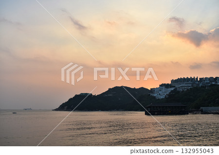 The seascape at sunset with ships and cityscape in the background. Sun-rays reflected on the calm sea. Sea background and cityscape. Nature concept. 132955043