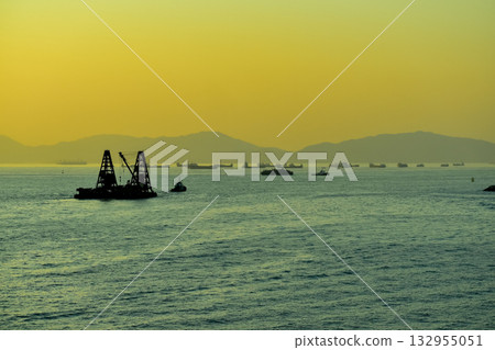 The seascape at sunset with ships and cityscape in the background. Sun-rays reflected on the calm sea. Sea background and cityscape. Nature concept. 132955051
