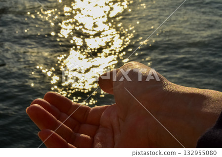 A male hand is opening to try to hold the sparkles in the sea. Nature concept. 132955080