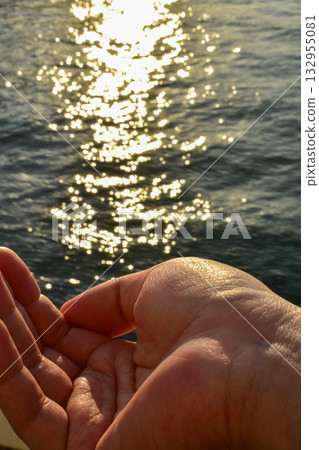 A male hand is opening to try to hold the sparkles in the sea. Nature concept. 132955081