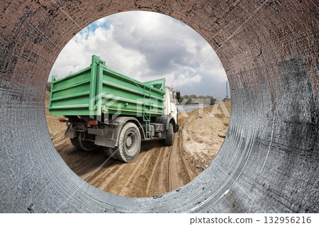 Heavy construction equipment is seen from a pipe, adding to the bustling activity on the site while clouds drift above in an open sky 132956216