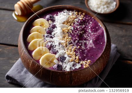 A vibrant purple acai bowl, garnished with coconut flakes, sliced bananas, and a drizzle of honey, promoting superfood benefits. 132956919