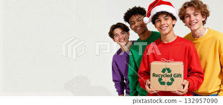 Diverse group of teenage friends celebrating Christmas with a recycled gift. Happy young men in colorful sweatshirts and a santa hat smiling together. Sustainable holiday banner with copy space 132957090