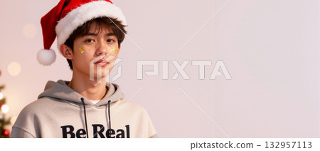 Young Asian man in a Santa hat with festive glitter makeup. Modern Christmas holiday portrait with copy space 132957113