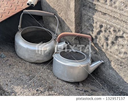 Two worn-out aluminum kettles on a concrete roadside Two worn-out aluminum kettles on a concrete roadside 132957137